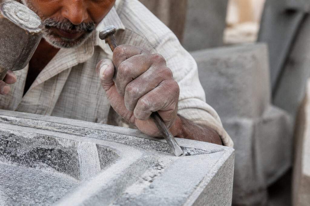 Un artisan sculpte une pierre tombale avec un ciseau et un maillet dans un atelier.